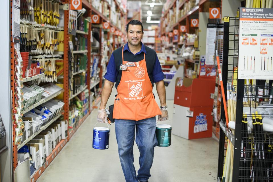 Home Depot associate carrying paint buckets down a store aisle