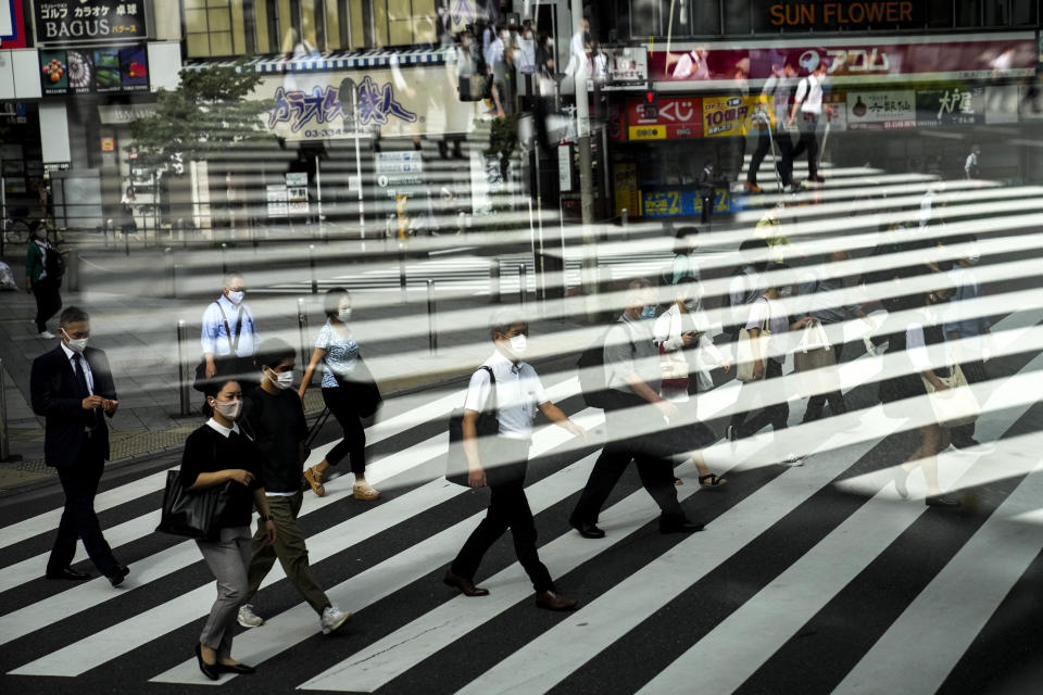 Commuters are reflected in a bus window as they cross the street Thursday, July 15, 2021, in Tokyo. The pandemic-delayed 2020 Summer Olympics open on July 23 without spectators at most venues. (AP Photo/Jae C. Hong)