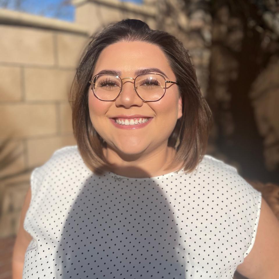 Woman smiling in sunlight, wearing glasses, and a dotted top