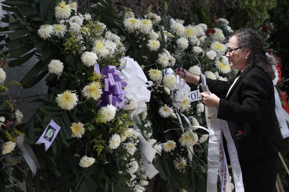 A woman places a ribbon on a flower arrangement, at the funeral of elementary school principal Elsa Mendoza, of one of the 22 people killed in a shooting at a Walmart in El Paso, in Ciudad Juarez, Mexico, Thursday, Aug. 8, 2019. Mexican officials have said eight of the people killed in Saturday's attack were Mexican nationals. (AP Photo/Christian Chavez)