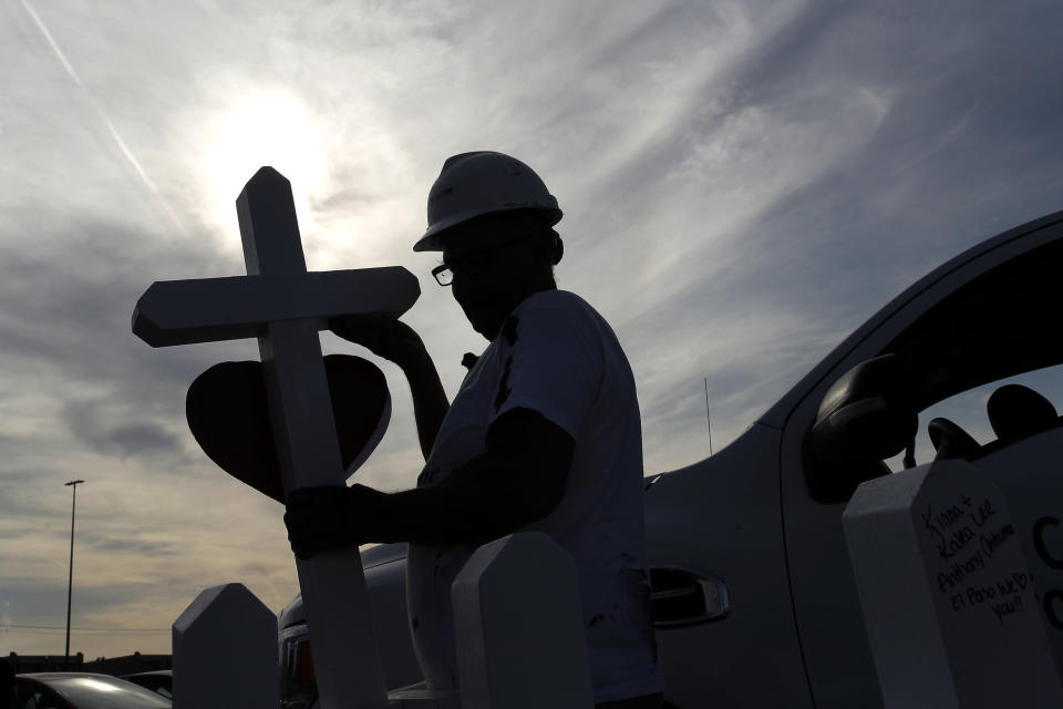 FILE - In this Aug. 5, 2019, file photo, Greg Zanis, of Aurora, Ill., stands in silhouette as he prepares crosses to place in memory of victims at a makeshift memorial for victims of a mass shooting at a shopping complex in El Paso, Texas. Now on hospice care, Zanis, continues to struggle against the terminal bladder cancer he was diagnosed with in March, was treated to a motorcade of well-wishers in his driveway for over two hours, Friday, May 1, 2020, in Aurora. (AP Photo/John Locher, File)