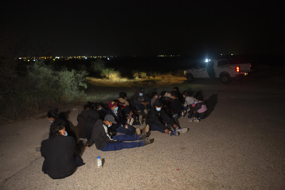 Migrants, mostly from Guatemala, wait at a U.S. Border Patrol intake site after they were smuggled on an inflatable raft across the Rio Grande river in Roma, Texas, Wednesday, March 24, 2021. On Wednesday, President Joe Biden tapped Vice President Kamala Harris to lead the White House efforts at the U.S. southern border and work with Central American nations to address root causes of the migration. The lights of the Mexican city of Miguel Aleman can be seen in the background. (AP Photo/Dario Lopez-Mills)