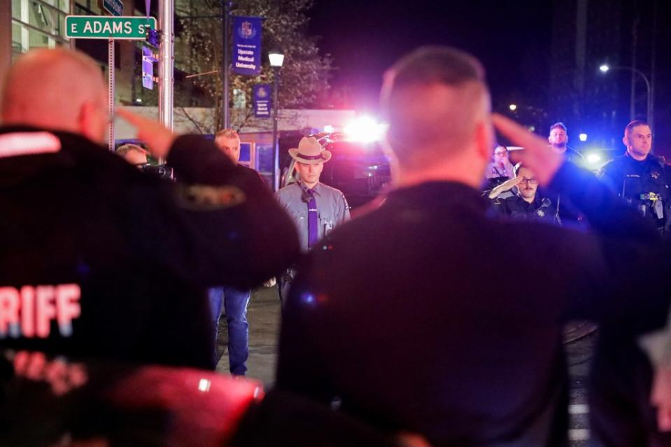 Hundreds of officers watch and salute as the bodies of the slain officer and deputy were driven away from Upstate Medical University Hospital. REUTERS