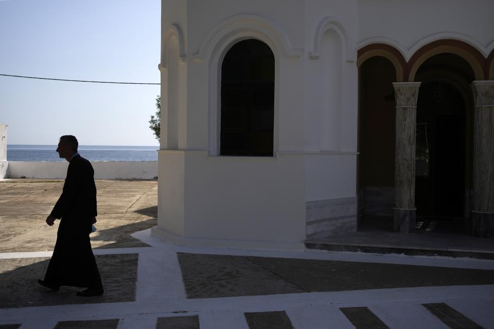 A Greek Orthodox priest walks in front of Agios Nikolaos church on the Aegean Sea island of Tilos, southeastern Greece, Tuesday, May 10, 2022. When deciding where to test green tech, Greek policymakers picked the remotest point on the map, tiny Tilos. Providing electricity and basic services, and even access by ferry is all a challenge for this island of just 500 year-round inhabitants. It's latest mission: Dealing with plastic. (AP Photo/Thanassis Stavrakis)