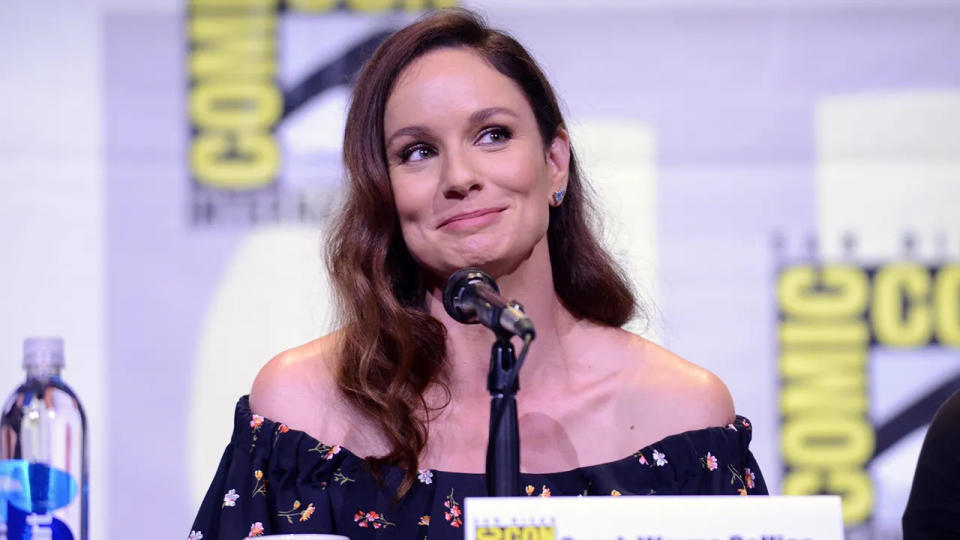 Sarah Wayne Callies in a patterned off-shoulder dress looks up on stage at Comic Con