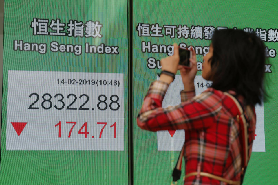 A woman takes a photograph in front of an electronic board showing Hong Kong share index outside a bank in Hong Kong, Thursday, Feb. 14, 2019. (AP Photo/Kin Cheung)
