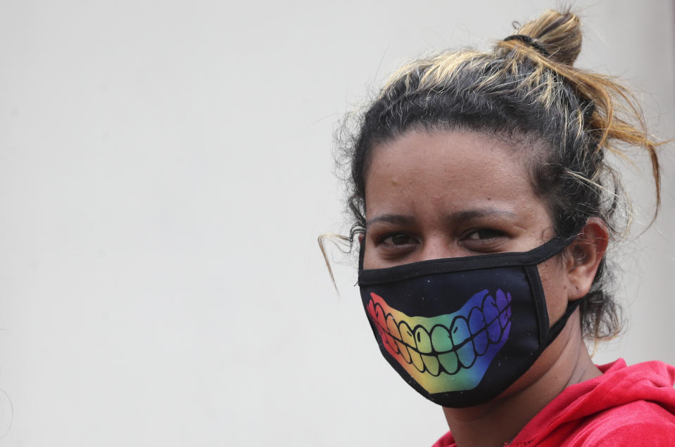 A woman, wearing a decorative, protective face mask as a precaution against the spread of the new coronavirus, eyes the camera as she walks past in Quito, Ecuador, Saturday, March 28, 2020. The government has declared a health emergency, enacting a curfew and restricting movement to only those who provide basic services. (AP Photo/Dolores Ochoa)