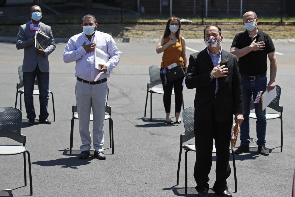 New citizens recite the Pledge of Allegiance while observing social distancing outside the U.S. Citizenship and Immigration Services building, Thursday, June 4, 2020, in Lawrence, Mass. The federal agency is resuming services in many cities across the country after being shuttered for more than two months because of the coronavirus pandemic. (AP Photo/Elise Amendola)