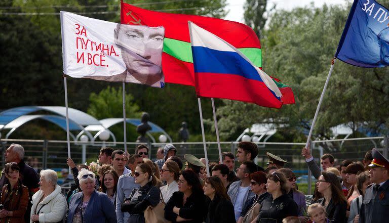 La gente lleva una bandera rusa y una bandera con un retrato del presidente ruso Vladimir Putin que dice 