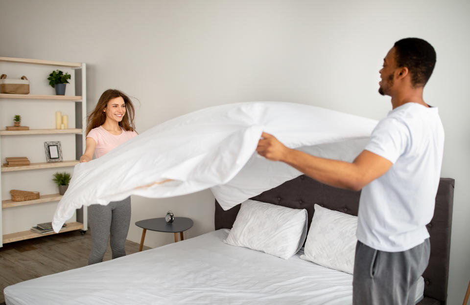 A man and woman changing their bed sheets together