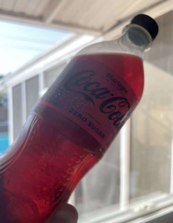 The bottle of Coke Starlight held up to a window, and you can see a ruby-colored tint to the liquid