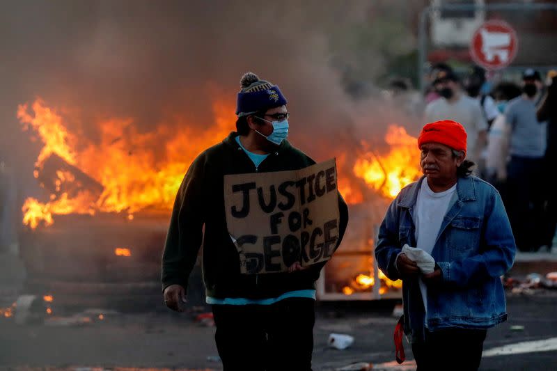 FILE PHOTO: A man wearing a face mask holds a sign near a burning vehicle at the parking lot of a Target store during protests in Minneapolis