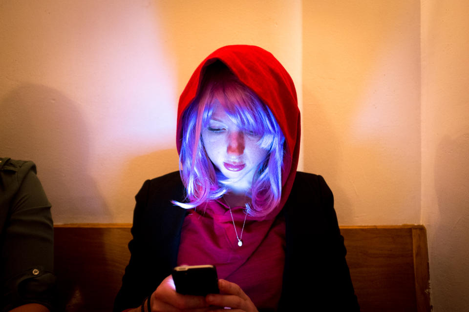Người phụ nữ đội tóc giả màu tím và đội mũ trùm đầu đỏ kiểm tra điện thoại ở thành phố New York, New York, Mỹ. (Ảnh của: Edwin Remsburg / VW Pics qua Getty Images)