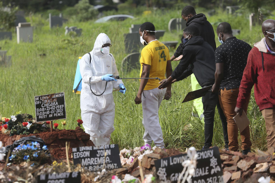 FILE - In this Jan. 15, 2021, file photo, a health worker disinfects family members during a burial of a person who died from COVID-19, in Harare, Zimbabwe. Africa has surpassed 100,000 confirmed deaths from COVID-19 as the continent praised for its early response to the pandemic now struggles with a dangerous resurgence and medical oxygen often runs desperately short. (AP Photo/Tsvangirayi Mukwazhi, File)