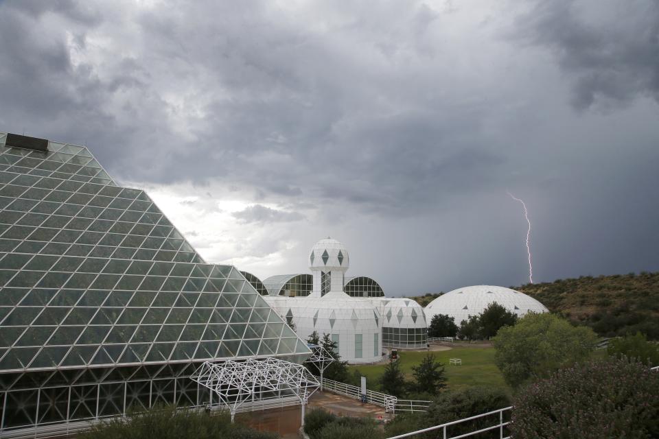 In this July 31, 2015 photo, several of the main buildings of the Biosphere 2 complex, including the tropical rainforest, left, the technosphere, middle, and the south lung, right, are shown as a thunderstorm moves past, in Oracle, Ariz. University of Arizona officials say that 25 years after that New Age-style experiment in the Arizona desert, the glass-covered greenhouse thrives as a singular site for researchers from around the world studying everything from the effects of the ocean’s acidification on coral to ways of ensuring food security. (AP Photo/Ross D. Franklin)