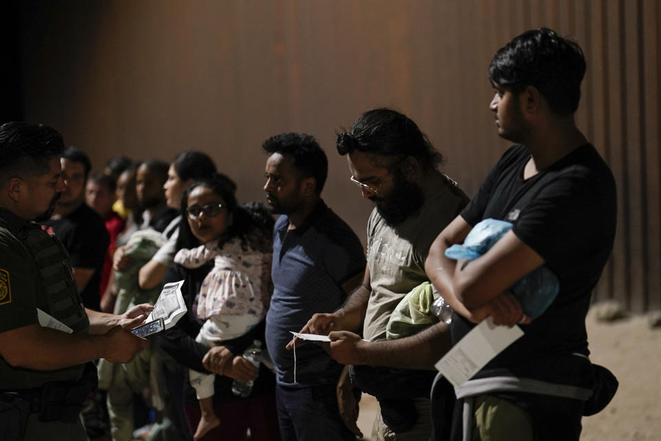 Migrants wait to be processed by Border Patrol agents near the end of a border wall Tuesday, Aug. 23, 2022, near Yuma, Arizona. The Border Patrol is seeing a dramatic shift in the type of migrants who come across the busiest places on the U.S.-Mexico. Migrants are now coming from more than 100 countries, and Mexicans are virtually absent. (AP Photo/Gregory Bull)