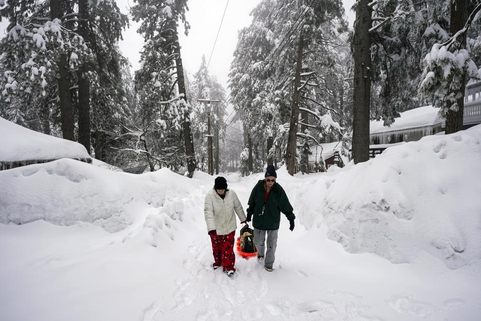 Angie Gourirand, right, and Cindy Maner, whose cars are buried in the snow, carry their groceries on a sled in Running Springs, Calif., Tuesday, Feb. 28, 2023. Beleaguered Californians got hit again Tuesday as a new winter storm moved into the already drenched and snow-plastered state, with blizzard warnings blanketing the Sierra Nevada and forecasters warning residents that any travel was dangerous. (AP Photo/Jae C. Hong)