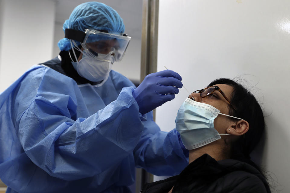 A nurse in protective clothing takes a swab from American Josephine Sandoval at a coronavirus testing center at the Rafik Hariri University Hospital in Beirut, Lebanon, Monday, Jan. 11, 2021. Lebanon's caretaker prime minister said Monday the country has entered a "very critical zone" in the battle against coronavirus as his government mulls tightening nationwide lockdown announced last week. (AP Photo/Bilal Hussein)