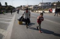 A boy and a man carry their belongings on their way to the new temporary refugee camp in Kara Tepe, near Mytilene the capital of the northeastern island of Lesbos, Greece, Thursday, Sept. 17, 2020. Greek police are moving hundreds of migrants to an army-built camp on the island of Lesbos Thursday after a fire destroyed an overcrowded facility, leaving them homeless for days. (AP Photo/Petros Giannakouris)