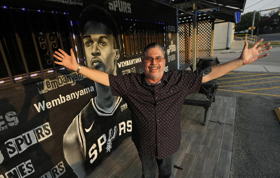 Businessman and San Antonio Spurs fan Roland Ramirez poses with a mural of Victor Wembanyama, a 7-foot-3 French basketball star, that artist Nik Soupe painted on the side of his seafood restaurant in San Antonio, Thursday, June 15, 2023. The San Antonio Spurs are expected to make Wembanyama the No. 1 pick in the NBA draft. (AP Photo/Eric Gay)