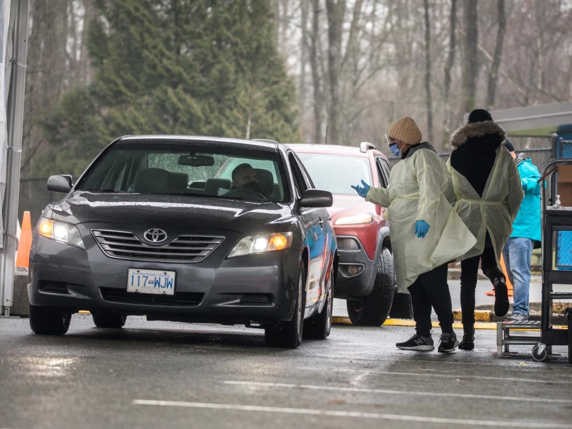 A health-care worker hands out COVID-19 rapid tests to people at the Bear Creek rapid test distribution centre in Surrey, B.C., on Jan. 18.  (Ben Nelms/CBC - image credit)