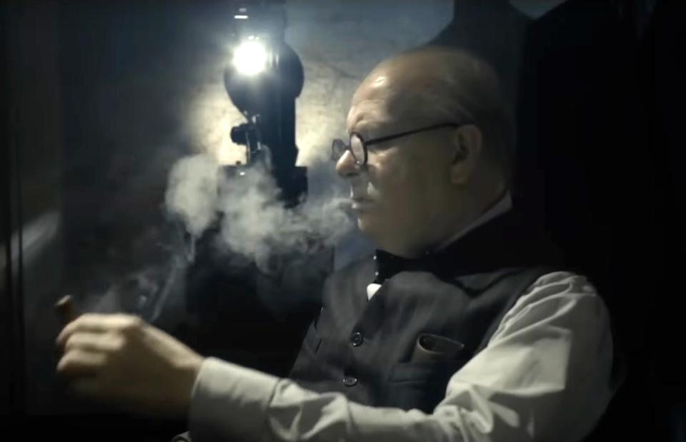 Gary in a suit smokes a cigar in a dimly lit setting