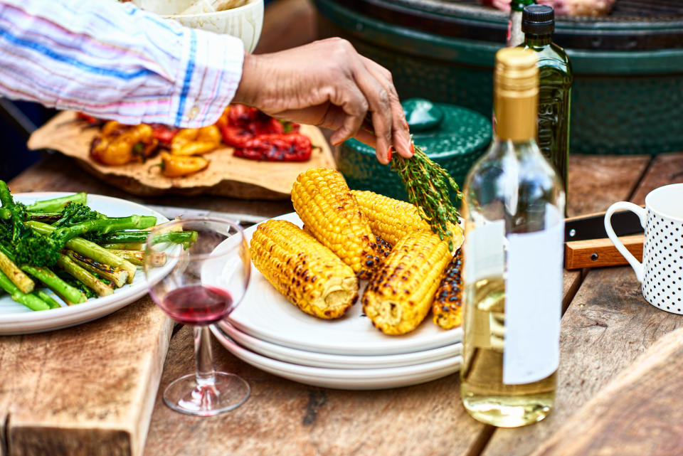 hand placing herbs over corn on the cob