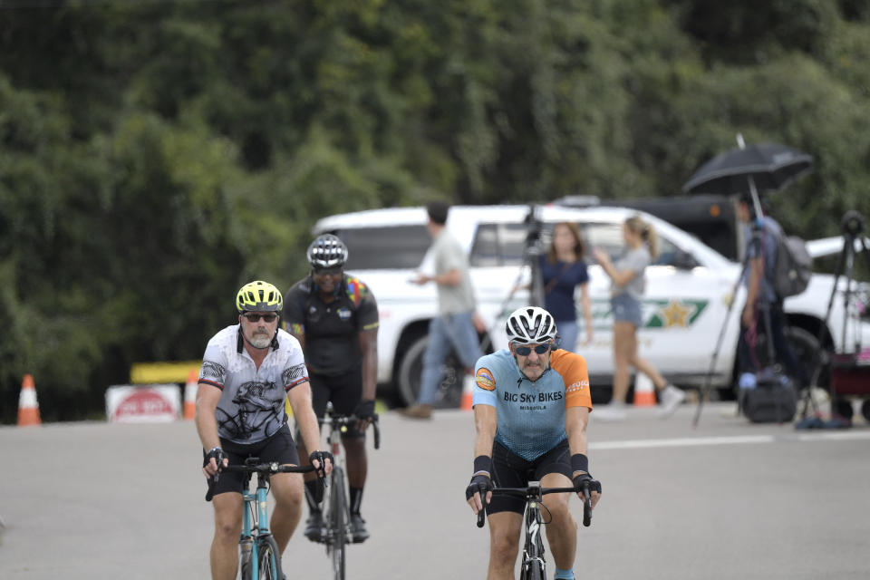 Bicyclists ride past television news reporters and a Sarasota County Sheriff's deputy stationed at the entrance of Carlton Reserve during a search for Brian Laundrie, Tuesday, Sept. 21, 2021, in Venice, Fla. Laundrie is a person of interest in the disappearance of his girlfriend, Gabrielle "Gabby" Petito. (AP Photo/Phelan M. Ebenhack)