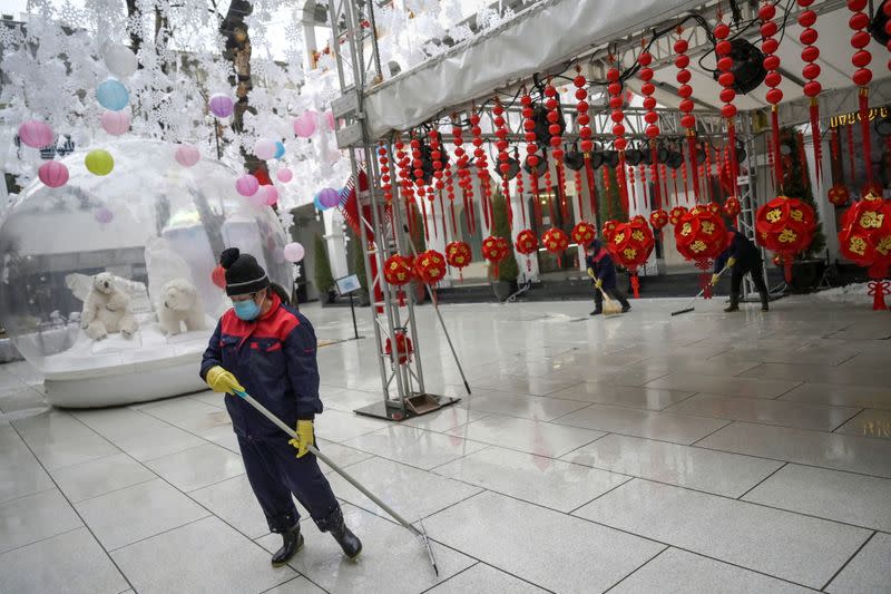 Worker wearing a face mask cleans the ground of a food court amid snowfall on Valentine's Day at the Sanlitun shopping area