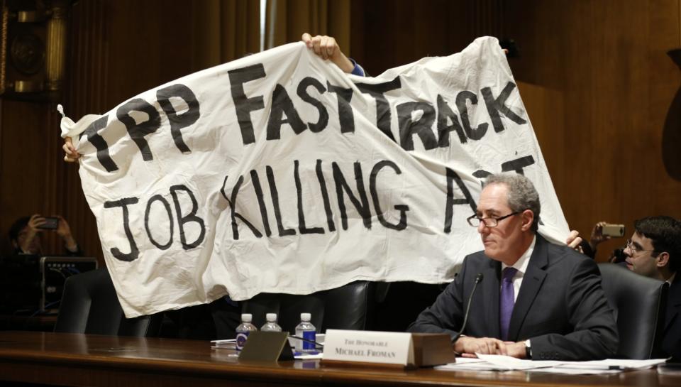 Trans-Pacific Partnership (TPP: Man holds a sign over U.S. Trade Representative Michael Froman (R) as he testifies before a Senate Finance Committee hearing on 