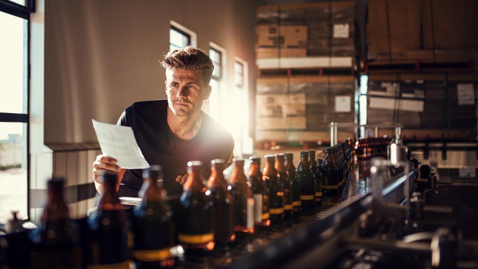 Young man supervising the process of beer manufacturing on brewery factory.