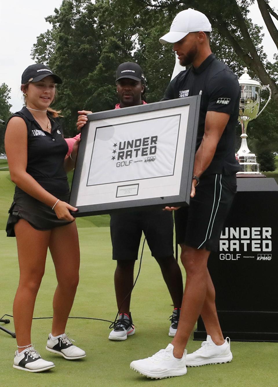 Julia Vollmer, top female on the Akron stop of Underrated Golf tour, takes the framed flag from Stephen Curry on 18th green of the South Course at Firestone Country Club in Akron.