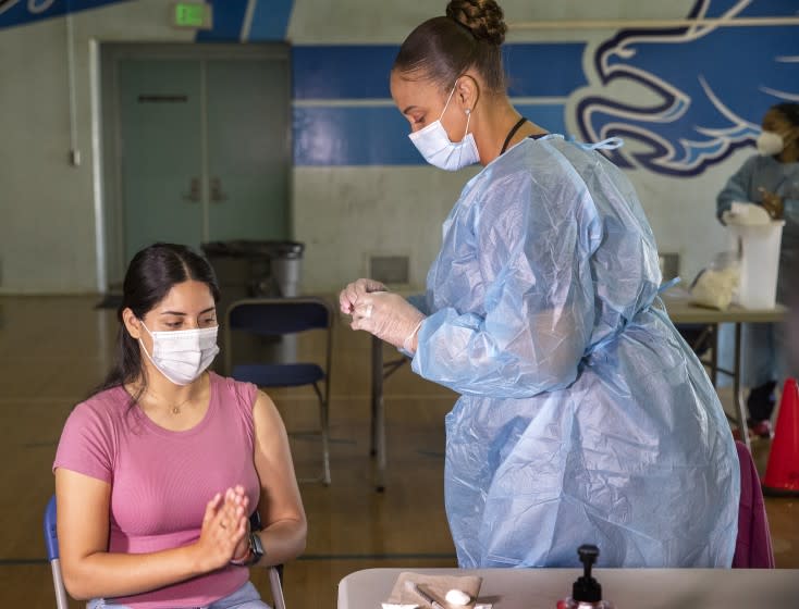 SAN FERNANDO, CA - AUGUST 30, 2021: Angela Saveva, 21, a teacher's assistant at San Fernando Middle School in San Fernando, is thankful after receiving the first dose of the Pfizer vaccine from Tracy Jones, a licensed vocational nurse. A mobile COVID-19 vaccine clinic was set up inside the gymnasium at San Fernando Middle School to inoculate LAUSD employees and students age 12 and older. (Mel Melcon / Los Angeles Times)