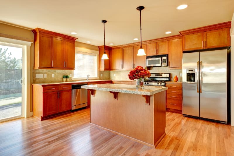 Bright kitchen with narrow plank hardwood floor, wood cabinets, modern steel appliances and tile back splash