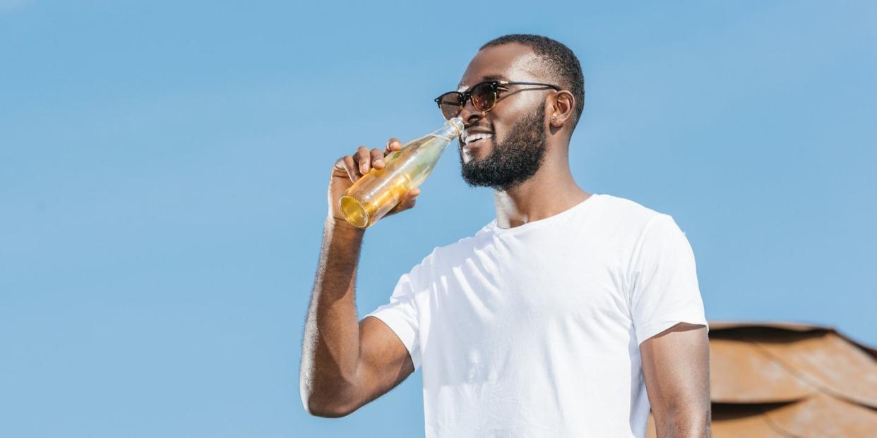 smiling handsome african american man drinking soda against blue sky