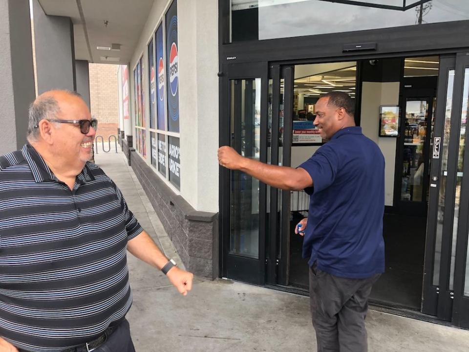 Two men greet each other outside a store.