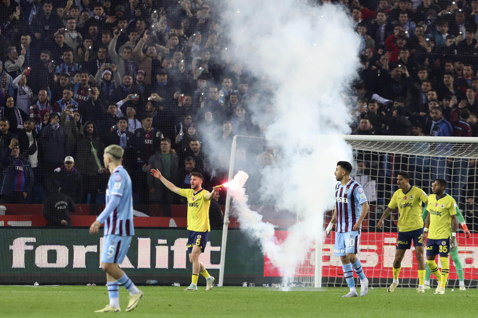 Fenerbahce's Ismail Yuksek holds a flare thrown by Trabzonspor supporters from the stand during the Turkish Super Lig soccer match between Trabzonspor and Fenerbahce at the Senol Gunes stadium in Trabzon, Turkey, Sunday, March 17, 2024. Turkish top tier club Trabzonspor fans invaded the pitch following a home loss against Fenerbahce late Sunday, touching off violent scuffles between the fans and Fenerbahce players. (Serkan Hacioglu/Dia Images via AP)