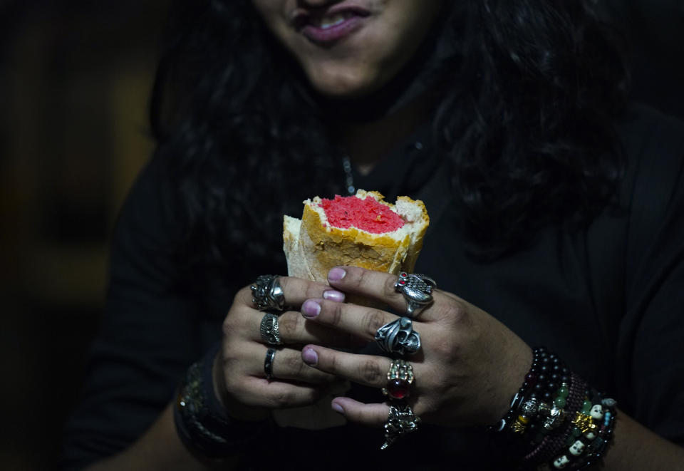 A youth who plays guitar in a rock band east a pink tamal before his show at a street tamales shop in downtown Mexico City, Thursday, Jan. 26, 2023. Vendors set up stands across the city before dawn at subway stops and street corners where tamales steam in giant pots fired by gas burners or charcoal. (AP Photo/Fernando Llano)