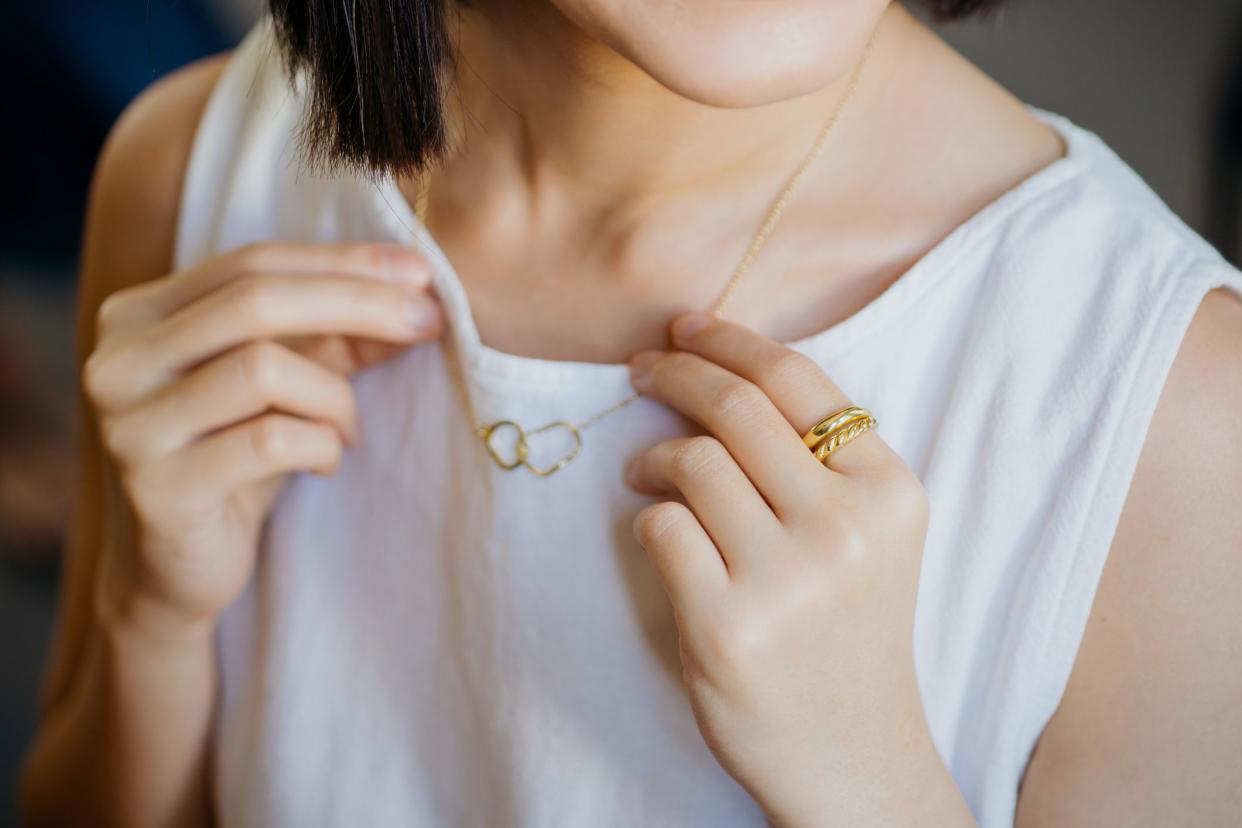 Close-up shot of portrait of a gorgeous young woman trying on a gold necklace at a jewelry and fashion shop