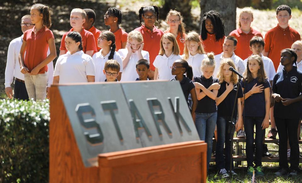 Children from the choir at nearby Joseph Finegan Elementary School (which is now known as Anchor Academy) stand silently during the rifle salute at the end of the 2017 memorial service for the USS Stark. A piece of the ship's stern bearing its name was on display during the ceremony.