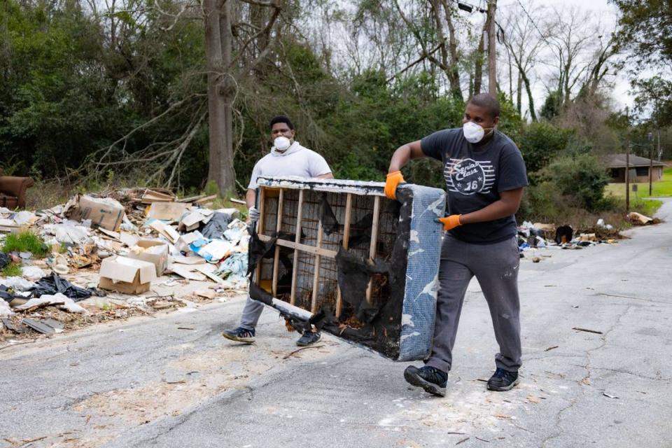 Volunteers carry a mattress to a dumpster during a cleanup of an illegal dump site in Macon.