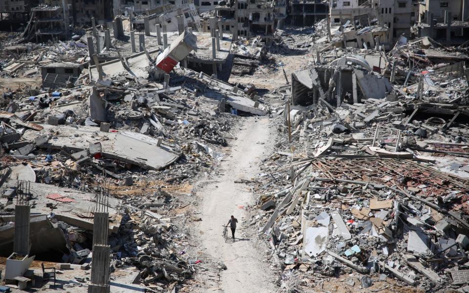 A man pushes a bicycle amid buildings transformed to rubble in the devastated area around Gaza's Al-Shifa hospital