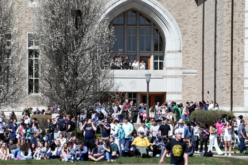 People stand at the DeBartolo Performing Arts Center and on the lawn as they watch the sky Monday, April 8, 2024, at the solar eclipse watch party on the Irish Green at the University of Notre Dame in South Bend.