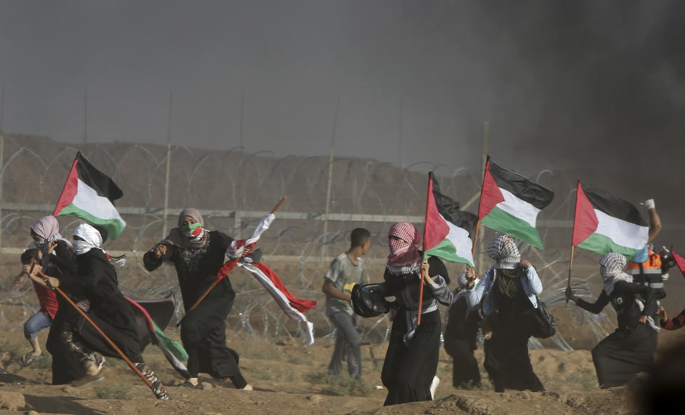 FILE - Female protesters wave Palestinian national flags as they run from teargas fired by Israeli troops, near fence of Gaza Strip border with Israel, during a protest east of Gaza City, Friday, Sept. 7, 2018. A teenager was killed and dozens of other Palestinians injured by Israeli fire at a border protest, Gaza officials said. Rights groups said Thursday. Dec. 2, 2021, that Israel failed to investigate shootings that killed more than 200 Palestinians and wounded thousands at violent protests along the Gaza frontier in recent years, strengthening the case for the International Criminal Court to intervene. (AP Photo/Adel Hana, File)