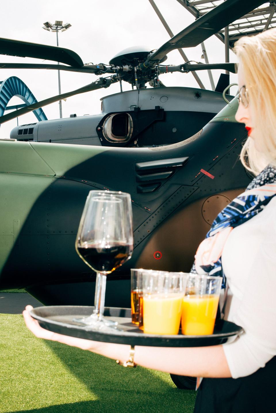 A woman holding tray of juice and wine in front of a military helicopter.