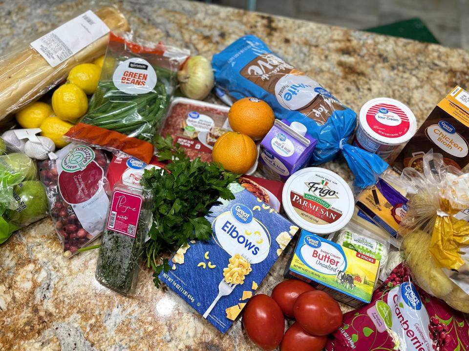 Groceries on kitchen counter including herbs, lemons, tomatoes, and bread