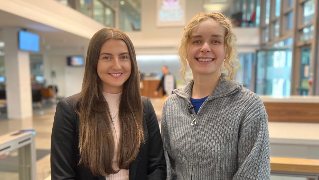 Two women, one with long dark and and the other with blonde curly hair smile at the camera