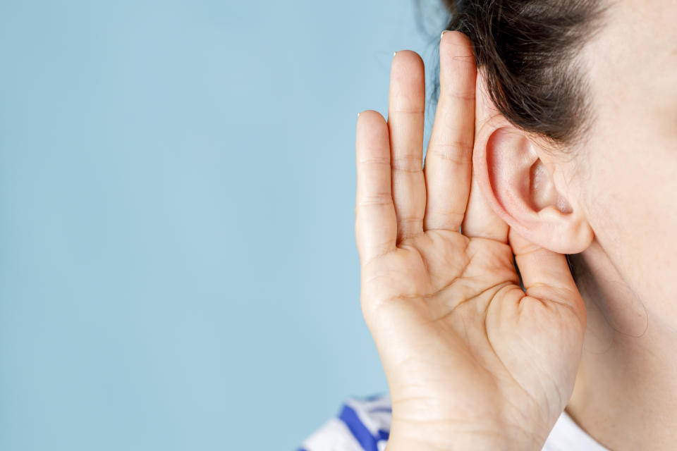 Young woman who has trouble hearing what the other person is saying. Damage from loud noises can lead to permanent hearing loss over time. (Getty) Hand is holding ear of woman to hear better