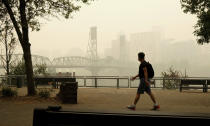 In this photo provided by Don Ryan, a pedestrian walks past the Willamette Bridge and downtown Portland, Ore., enveloped in heavy smoke from wildfires on Wednesday, Sept. 16, 2020. (Don Ryan via AP)