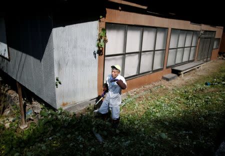 A local resident pauses as he pulls out the weeds at an empty house in Nanmoku Village, northwest of Tokyo, Japan October 12, 2017. Picture taken October 12, 2017. REUTERS/Issei Kato